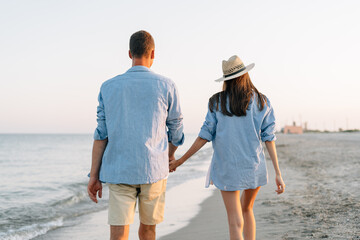 Rear view of young happy couple two friends family man woman in blue shirt clothes hold hands walk...