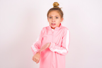 caucasian little kid girl with bun hairstyle wearing pink tracksuit over white background In hurry pointing to watch time, impatience, upset and angry for deadline delay.