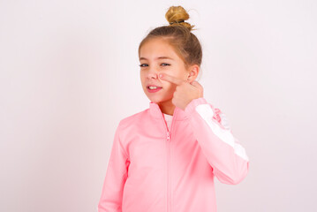 caucasian little kid girl with bun hairstyle wearing pink tracksuit over white background pointing...