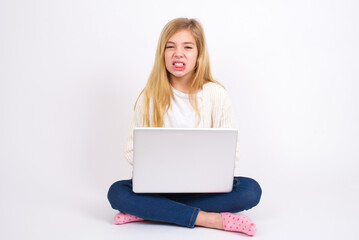 Naklejka premium Mad crazy caucasian teen girl sitting with laptop in lotus position on white background clenches teeth angrily, being annoyed with coming noise. Negative feeling concept.