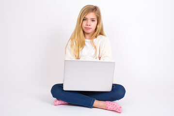 caucasian teen girl sitting with laptop in lotus position on white background bitting his mouth and looking worried and scared crossing arms, worry and doubt.