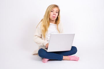 caucasian teen girl sitting with laptop in lotus position on white wall with snobbish expression curving lips and raising eyebrows, looking with doubtful and skeptical expression, suspect and doubt