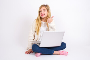 Fototapeta premium caucasian teen girl sitting with laptop in lotus position on white background giving thumb up gesture, good Job! Positive human emotion facial expression body language.