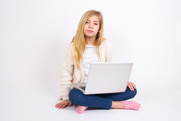 Fototapeta premium Happy caucasian teen girl sitting with laptop in lotus position on white background looking at camera with charming cute smile.