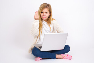 Fototapeta premium What the hell are you talking about. Shot of frustrated caucasian teen girl sitting with laptop in lotus position on white gesturing with raised hand doing Italian gesture, frowning, being displeased.