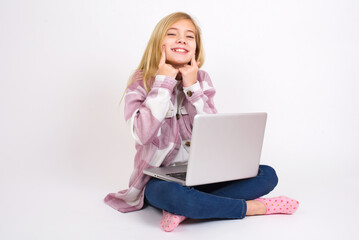 Strong healthy straight white teeth. Close up portrait of happy caucasian teen girl sitting with laptop in lotus position on white background with beaming smile pointing on perfect clear white teeth.