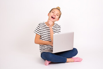 caucasian teen girl sitting with laptop in lotus position on white background stares aside with wondered expression has speechless expression. Embarrassed model looks in surprise