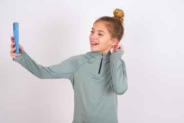 little caucasian kid girl with hair bun wearing technical shirt over white background smiling and...