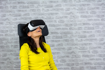 Middle aged woman in virtual reality (VR) glasses. Isolated on white grey wall background. Excited woman in VR headset touching air during virtual reality experience at studio. Emotional lady.