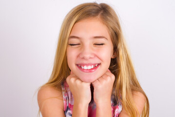 Cheerful little caucasian kid girl wearing sport clothing over white background has shy satisfied expression, smiles broadly, shows white teeth, People emotions