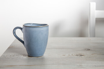 Fototapeta na wymiar A blue ceramic cup on a beige table against a white wall. Place for text. Copy space