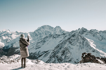 A girl on the top of Mount Elbrus takes pictures of the mountains during the day on her phone