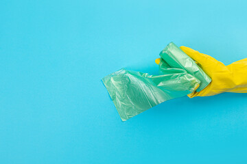 A hand in a yellow glove holds a plastic disposable trash bag on a blue background. place with copy space. Cleaning concept.