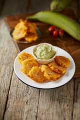 Patacones or tostones, typical Ecuadorian appetizer that consists on fried green plantain slices. It’s accompanied with guacamole and served on a traditional plate with a wooden and rustic background. © David