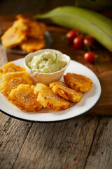 Patacones or tostones, typical Ecuadorian appetizer that consists on fried green plantain slices. It’s accompanied with guacamole and served on a traditional plate with a wooden and rustic background.