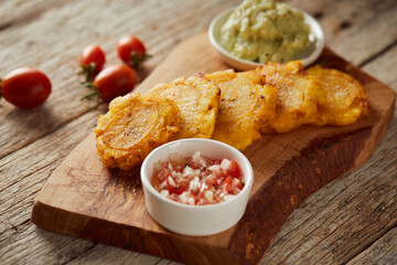 Patacones or tostones, typical Ecuadorian appetizer that consists on fried green plantain slices. It’s accompanied with guacamole and served on a traditional plate with a wooden and rustic background.