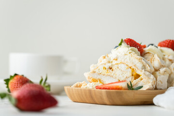 Meringue roll decorated with strawberries and blueberries sliced and served in the wooden plate on the white background. Macro shot