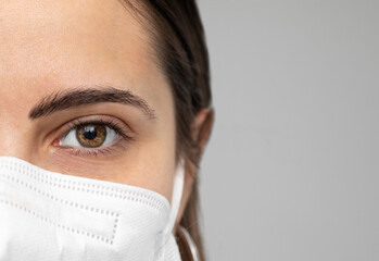 Close up of girl's brown eye with manicured eyebrows wearing a mask, neutral space for writing on the side