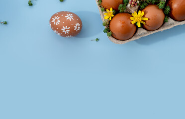 chicken eggs in a tray on a blue background with flowers, holiday concept, space for text