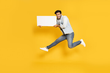 Fototapeta na wymiar Young man jumping and showing blank white billboard isolated on yellow background