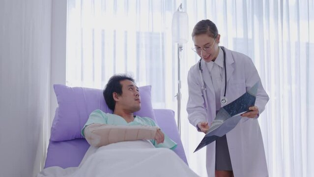 Female doctor holding an x-ray film consult male patient with broken arm lying in hospital bed. Medical professional Providing care and assistance to sick. Physician diagnose orthopedic treatments