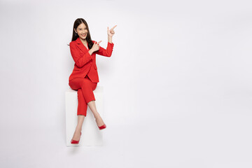 Young Asian businesswoman in red suit sitting and pointing to empty copy space isolated on white...