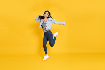 Fototapeta na wymiar Young Asian woman listening favourite music with wireless headphones and dancing isolated on yellow background