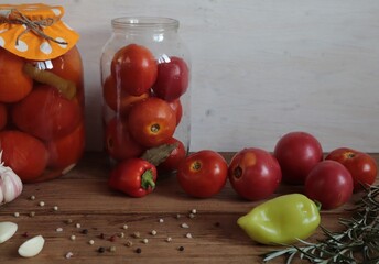 Red tomatoes with spices in glass jars and on a wooden surface.	