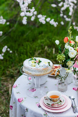 Tea time with cake and cookies in the spring garden outdoors. The table is covered with a floral tablecloth. In english style