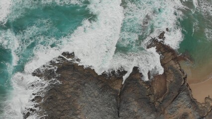 Crystal green waves crash against the stone coast of