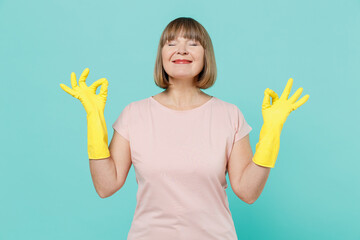 Elderly housewife woman 50s in pink t-shirt gloves spread hands in yoga om aum gesture relax...