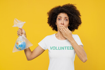 Young frightened sad woman of African American ethnicity in white volunteer t-shirt hold in plastic bag Earth world globe isolated on plain yellow background. Pollution greenhouse effect help concept.