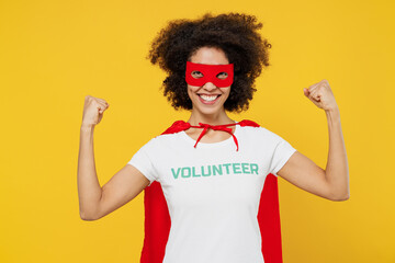 Young cool woman of African American ethnicity wears white volunteer t-shirt super hero costume do winner gesture isolated on plain yellow background Voluntary free work assistance help grace concept