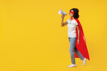 Full size young woman of African American ethnicity in white volunteer t-shirt super hero costume walk go scream megaphone isolated on plain yellow background. Voluntary free assistance help concept.