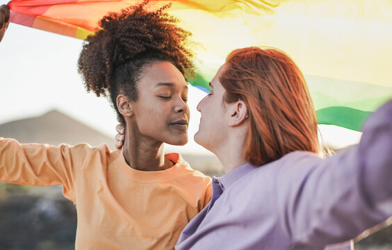Multiracial lesbian women holding LGBT rianbowflag outdoor while enjoy tender moment together