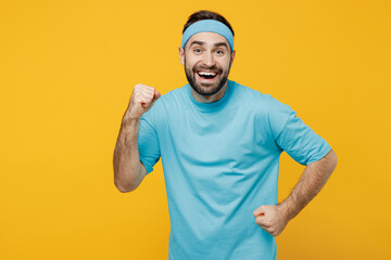 Young runner fitness trainer instructor sporty man sportsman in headband blue t-shirt spend weekend in home gym do winner gesture isolated on plain yellow background. Workout sport motivation concept.