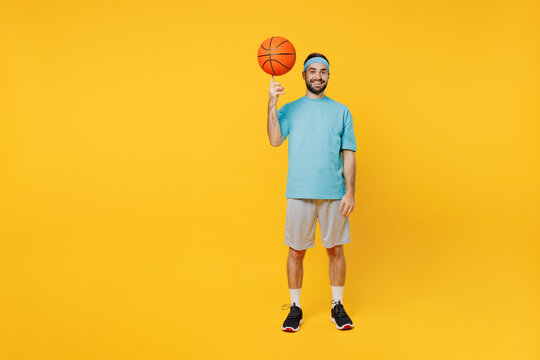 Full Body Fun Young Fitness Trainer Instructor Sporty Man Sportsman In Headband Blue T-shirt Spend Leisure Time In Gym Spin Basketball Ball Isolated On Plain Yellow Background. Workout Sport Concept.