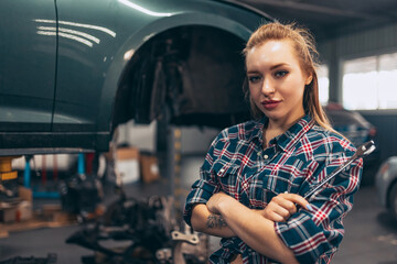 Fototapeta na wymiar Destroying gender stereotypes. Young woman auto mechanic working at auto service station using different work tools. Gender equality. Work, occupation, car