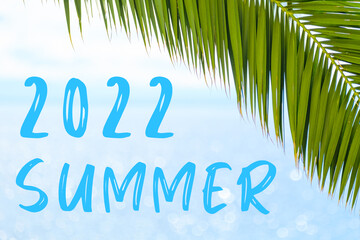 2022 summer text on the background with palm leaf and blue sea. Template of a greeting card, postcard or advertisement of a tour agency. 