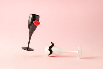 Creative layout made of black wineglass with red lips and white wineglass with mustache against pink background. Minimal love and party concept. Celebration anniversary composition.