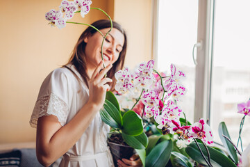 Happy woman enjoys blooming white orchid holding pot. Girl gardener taking care of home plants and...