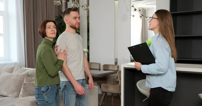 Young couple viewing new property and ready to become homeowners. Real estate agent welcomes in new apartment.