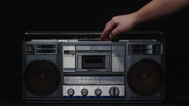 A man's hand inserts a cassette into a tape recorder and presses the play button