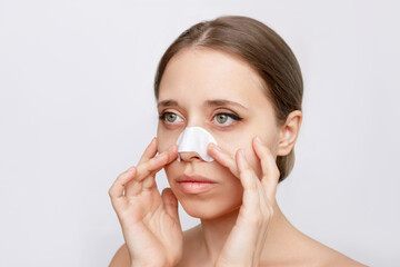 Portrait of a woman cleaning the skin of a face with nose strips from blackheads or black dots isolated on a white background. Acne problem, comedones. Enlarged pores on the face. Cosmetology concept