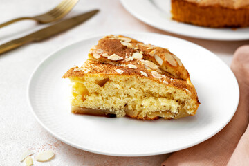 A piece of apple pie on a white plate on a light culinary background. Pie with charlotte on a platter closeup. Delicious homemade pastry on the kitchen table
