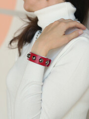 leather studded red bracelet on woman hand closeup photo on white wall background