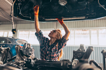 Portrait of beautiful young red-headed girl, auto mechanic at auto service station using different work tools for car examining. Gender equality. Work, occupation, car