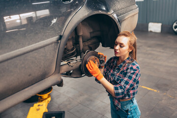Female auto mechanic. beautiful young red-headed girl in working process at auto service station,...