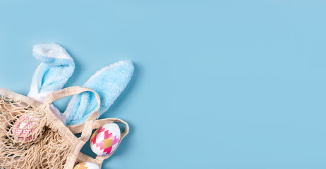 Wide banner on a blue background. The concept of online shopping for Easter, purchases and sale for the holiday. Gift bag with bunny ears and Easter eggs.