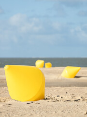 Four yellow buoys on a beach at low tide under a blue sky